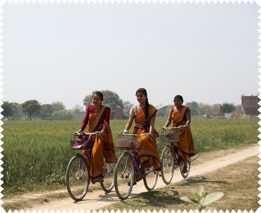 Die Kolleginnen in Indien fahren mit dem Rad durch eine ländliche Gegend zur Arbeit.